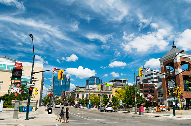 Traffic light intersection with buildings in the background and two people crossing the road.