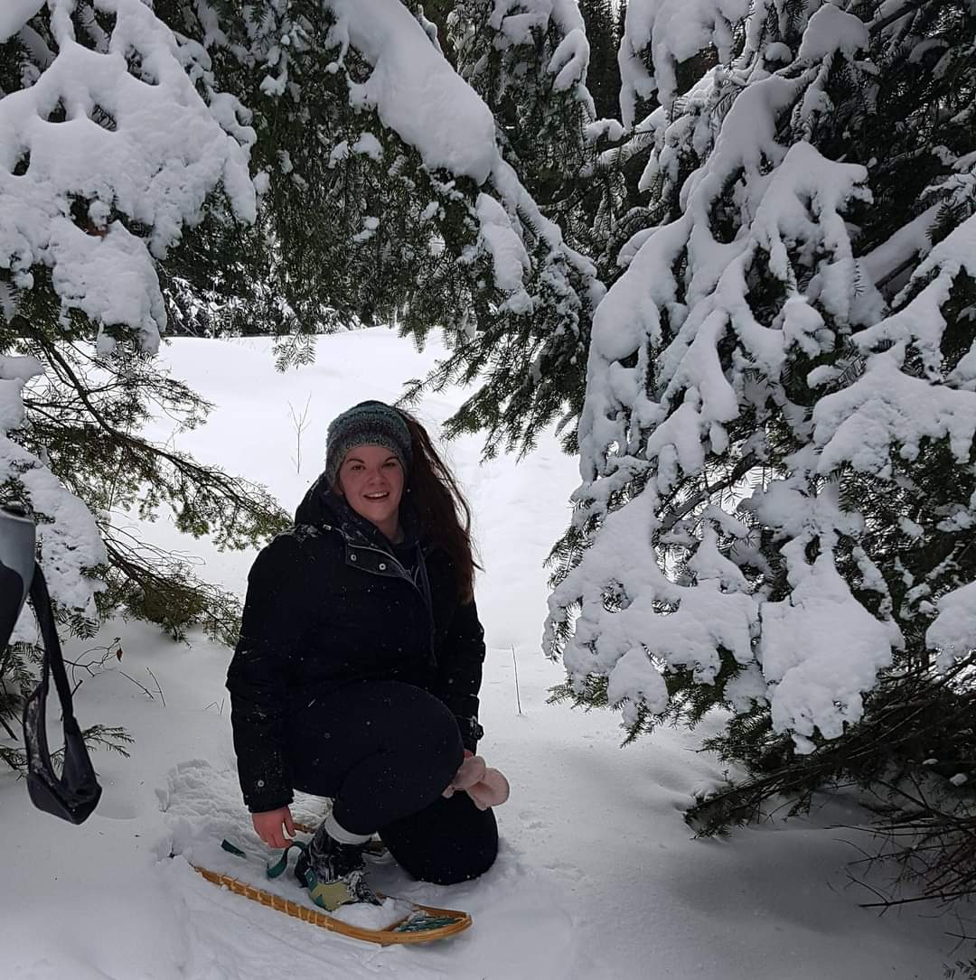 Aysha McNally in the snow next to pine trees