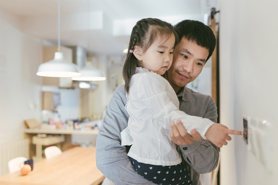 Father holding child near a thermostat in a house